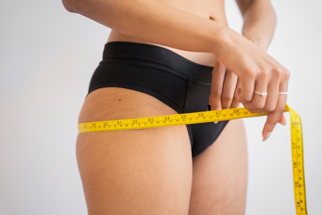 close-up of woman in black panties measuring her waist with yellow tape measure